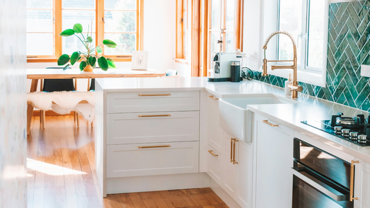 Minimalist kitchen with brass handles, emerald-tiled backsplash, and hardwood flooring