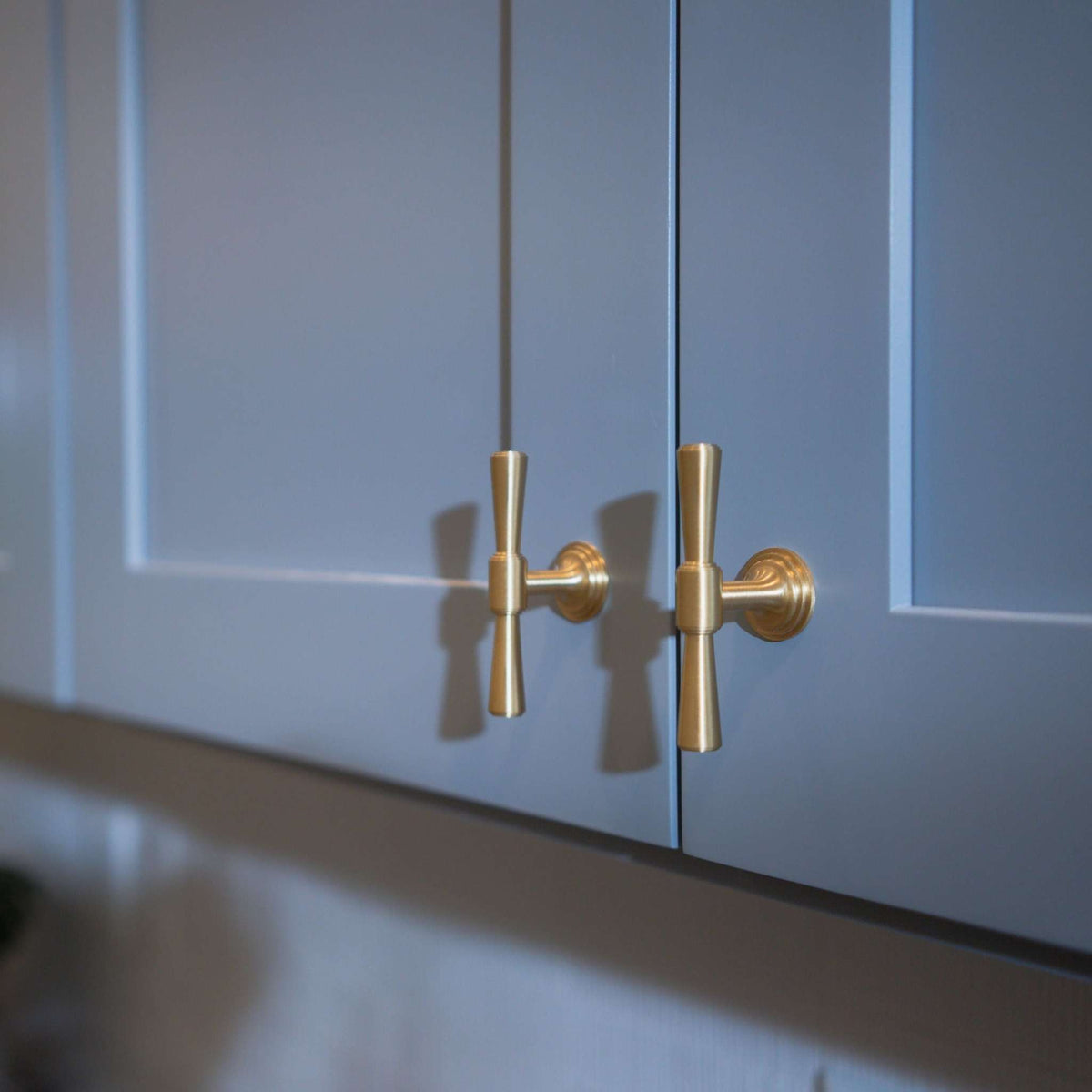 Two tapered T-shaped brass-colored knobs on blue cabinet doors.