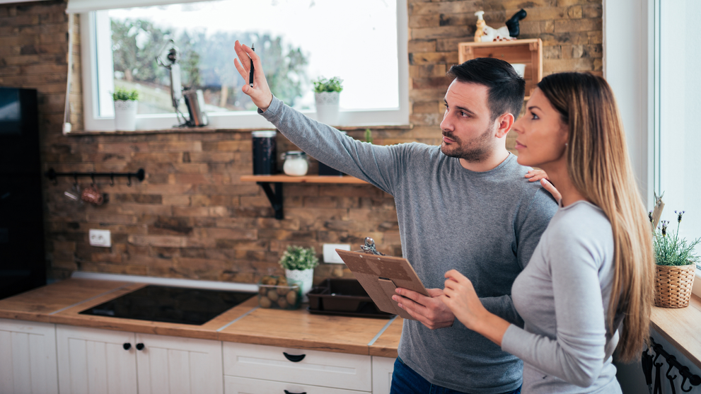 Couple Reviewing A Kitchen Renovation Checklist In A Modern Rustic Kitchen With Wood Countertops And Brick Backsplash
