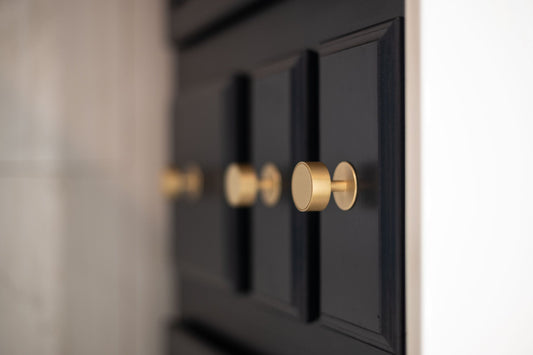 Close view of a Gateau brass knob on a dark bathroom vanity door