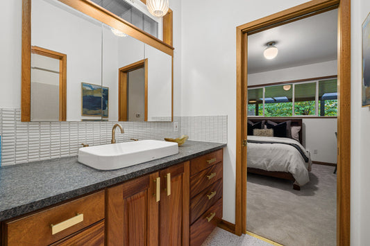 Wood bathroom vanity with brass Auburn pulls beneath a white vessel sink