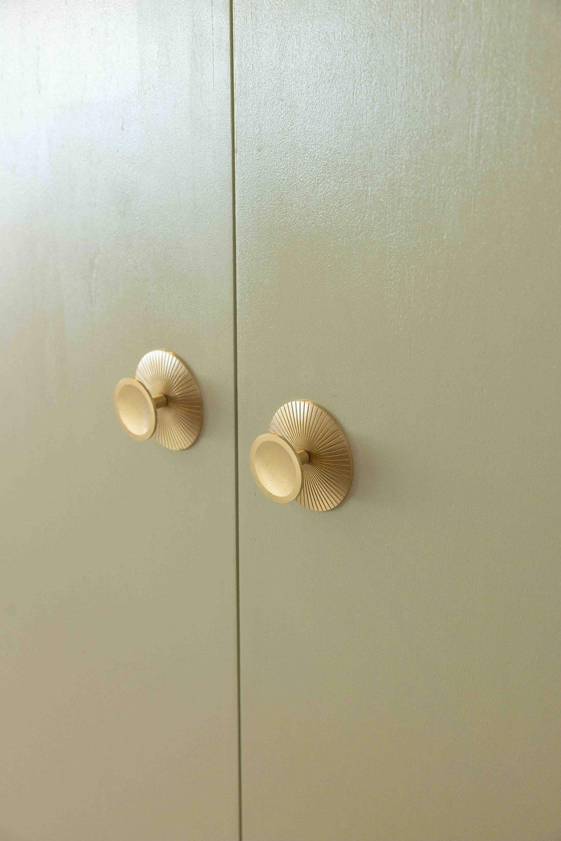 Paired Sunburst brass knobs on pale green cabinet doors