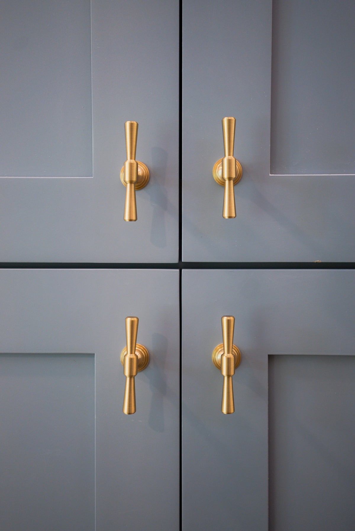 Four blue-gray cabinet doors with aligned Tuxedo brass knobs