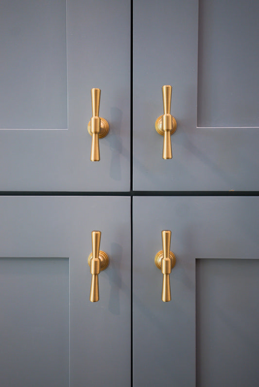 Four blue-gray cabinet doors with aligned Tuxedo brass knobs