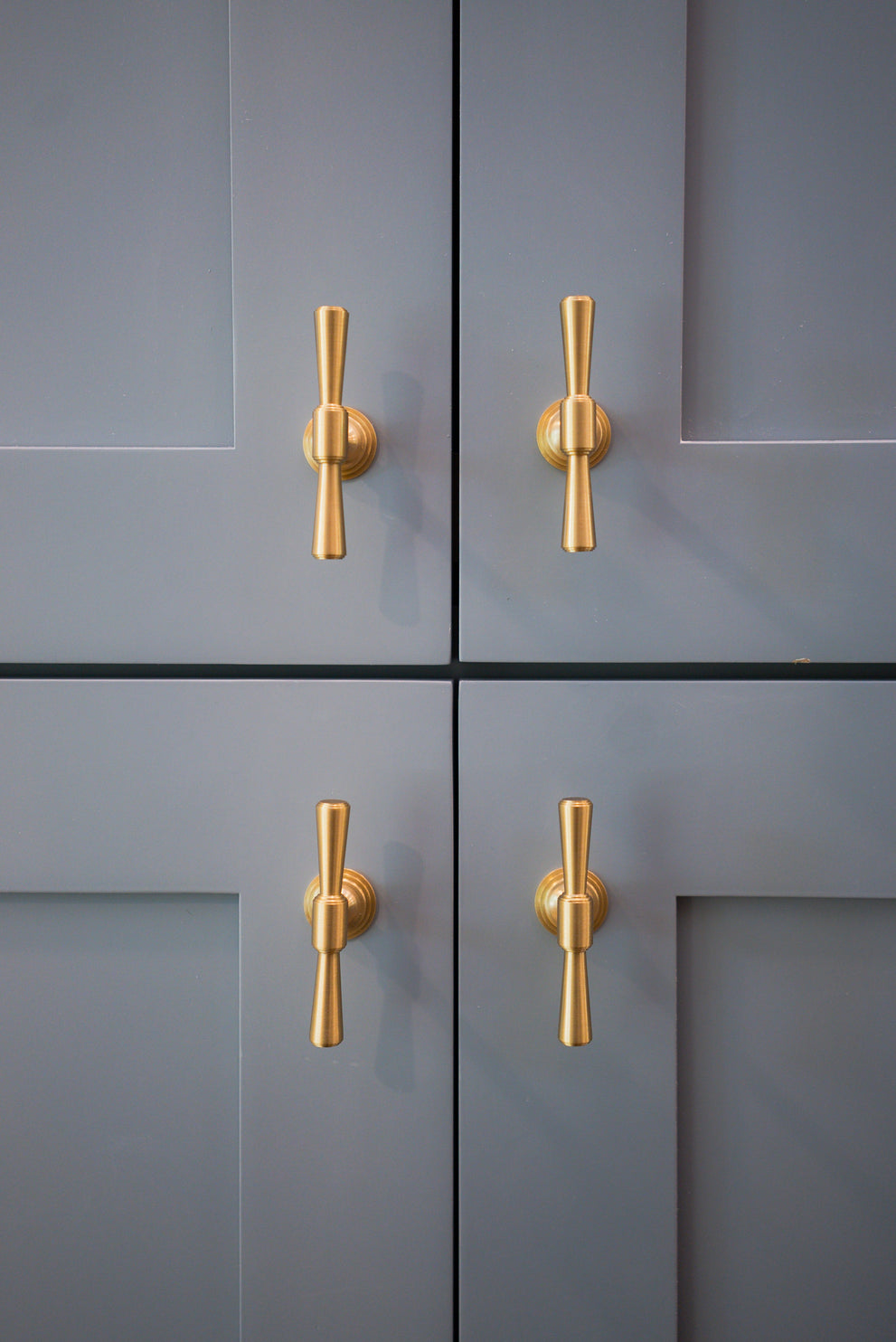 Four blue-gray cabinet doors with aligned Tuxedo brass knobs