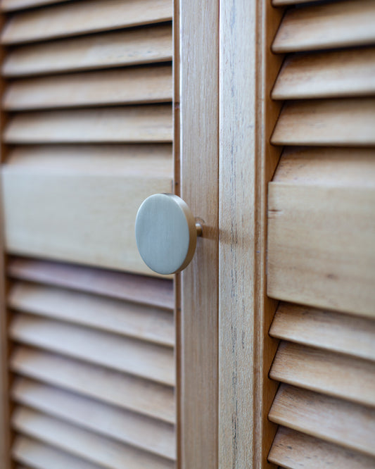 Flat round Rondelle knob mounted on a louvered wood cabinet door