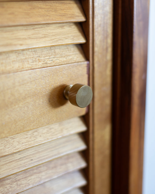 Brass Sunbeam knob with straight vertical fluting on a wood cabinet door