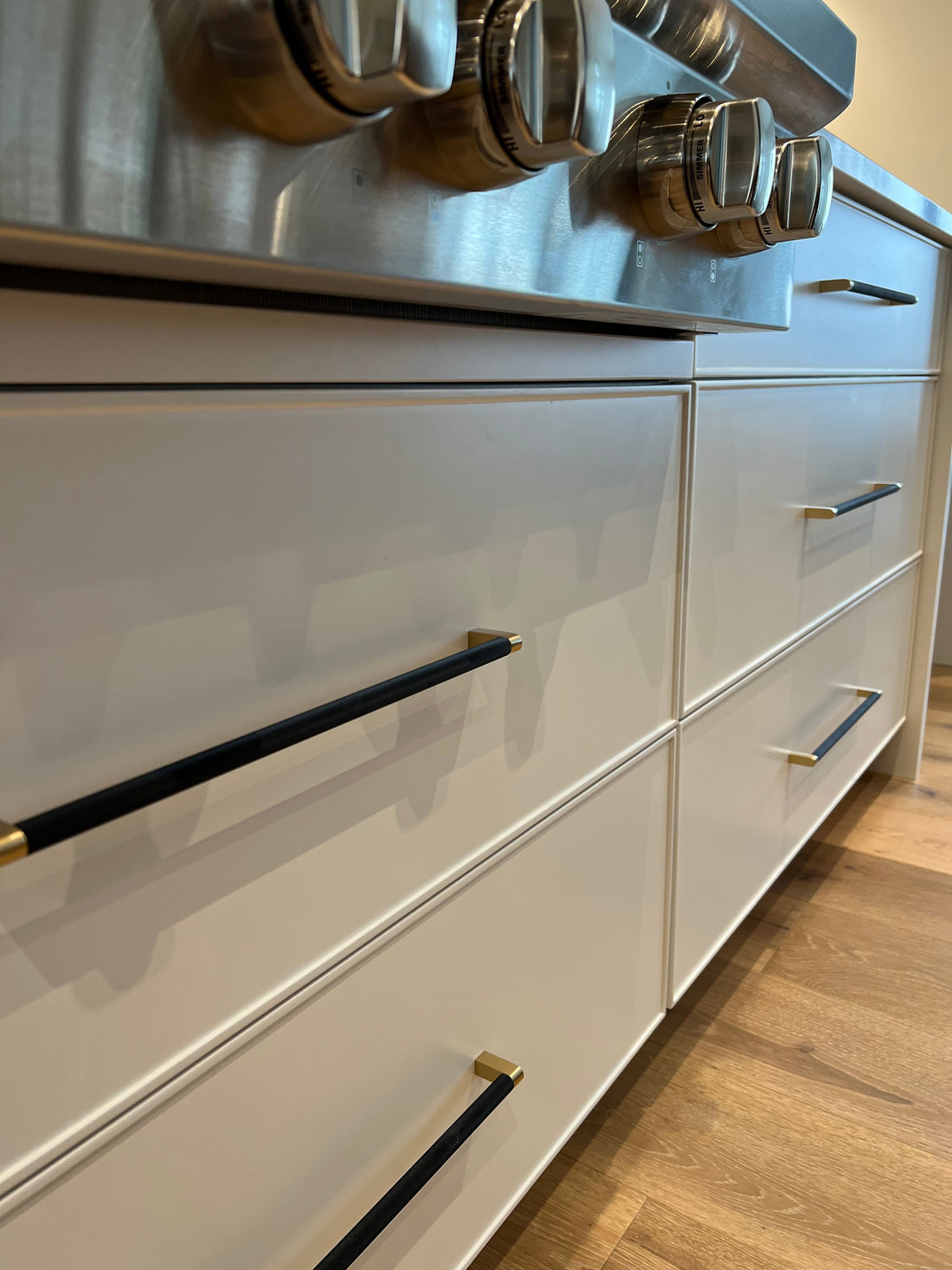 White kitchen drawers with black and brass Bold pulls beneath a stainless range