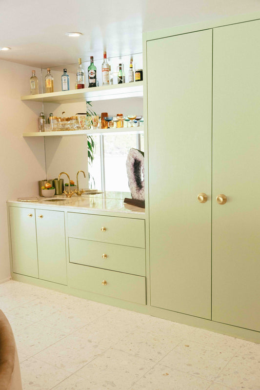 Pale green built-in cabinetry with Sunburst brass knobs on its tall doors