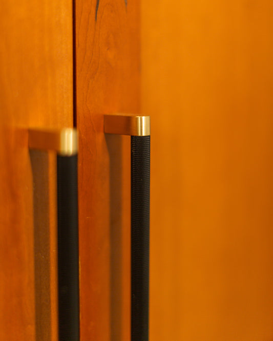 Close view of black knurled Bold cabinet pulls with brass feet on wood doors