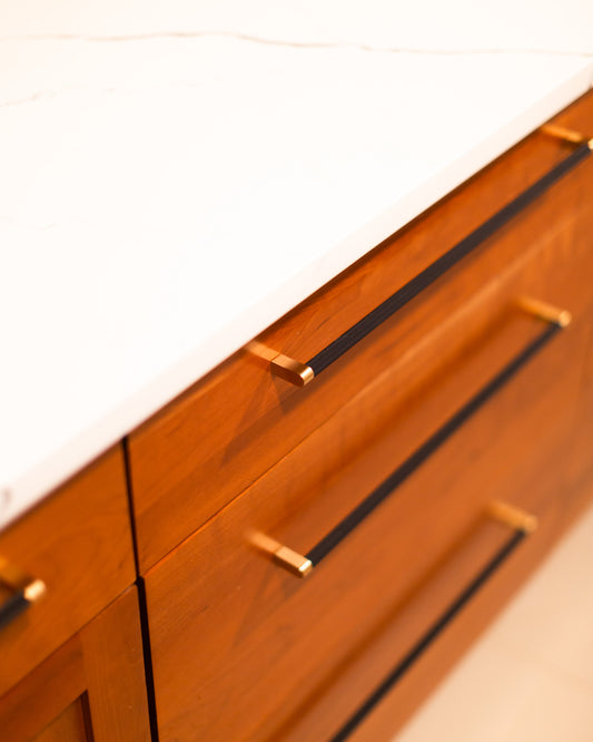 Bold black and brass pulls on flat wood drawers beneath a light counter
