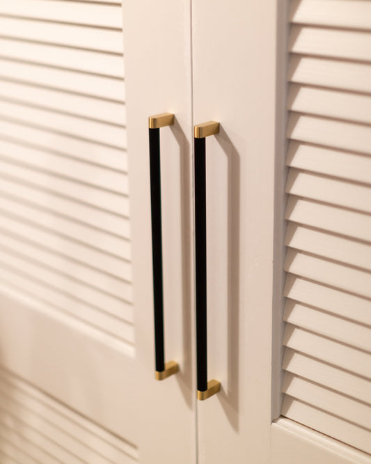 Bold black and brass cabinet pulls on white louvered doors